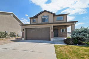 View of front of home with concrete driveway, brick siding, a garage, covered porch, and stucco siding