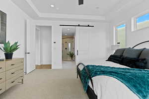 Bedroom with a barn door, a tray ceiling, recessed lighting, light carpet, and ceiling fan