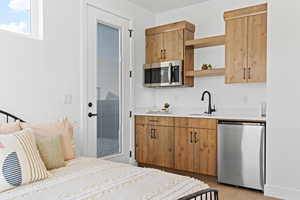 Kitchen with open shelves, appliances with stainless steel finishes, light wood finished floors, light stone countertops, and brown cabinets