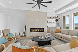 Living area featuring a tray ceiling, a tile fireplace, recessed lighting, wood finished floors, and ceiling fan