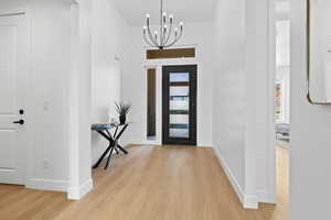 Entryway with light wood-style floors, a chandelier, and a high ceiling