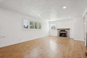 Unfurnished living room with recessed lighting, a premium fireplace, light wood finished floors, and a textured ceiling