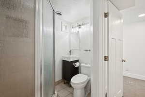 Full bathroom with vanity, a textured ceiling, a stall shower, and tile patterned flooring