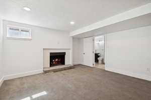 Unfurnished living room featuring carpet flooring, a fireplace, recessed lighting, and a textured ceiling