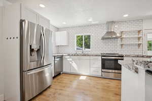 Kitchen featuring appliances with stainless steel finishes, wall chimney exhaust hood, decorative backsplash, white cabinetry, and recessed lighting