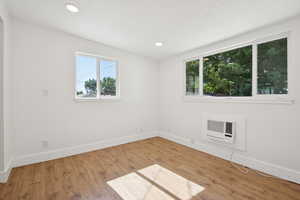Spare room with wood finished floors, an AC wall unit, and recessed lighting