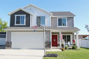 View of front facade with covered porch, concrete driveway, stone siding, and an attached garage