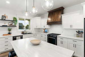 Kitchen featuring black range with gas cooktop, light countertops, white cabinets, and custom range hood
