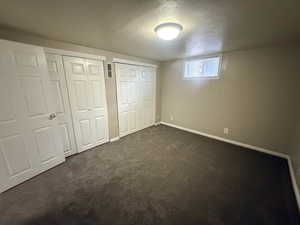 Unfurnished bedroom with a textured ceiling, multiple closets, and dark carpet