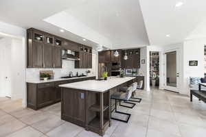 Kitchen featuring appliances with stainless steel finishes, wall chimney exhaust hood, light countertops, dark brown cabinetry, and light tile patterned floors