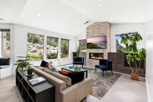 Living room with a stone fireplace, light tile patterned flooring, recessed lighting, and high vaulted ceiling