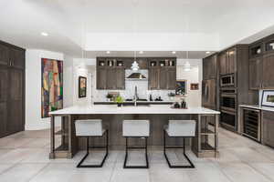 Kitchen featuring beverage cooler, appliances with stainless steel finishes, light countertops, a breakfast bar, and recessed lighting