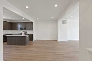 Kitchen featuring recessed lighting, dark brown cabinets, light countertops, light wood finished floors, and stainless steel microwave