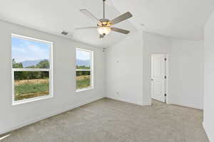 Carpeted spare room featuring a mountain view, lofted ceiling, and a ceiling fan
