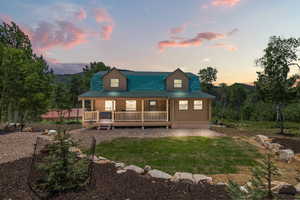 Back of house at dusk featuring covered porch and a yard