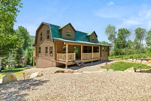Cabin with a porch, log exterior, a gambrel roof, and a front yard