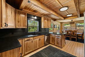 Kitchen with a peninsula, dark countertops, stainless steel dishwasher, light wood-style floors, and a wooden ceiling with exposed beams