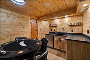 Bar featuring wooden walls, wooden ceiling, fridge, and light wood-type flooring