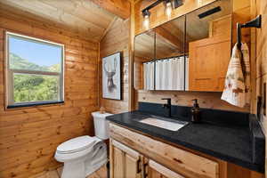 Bathroom with vaulted ceiling, vanity, wood walls, a shower with shower curtain, and wood ceiling