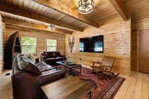 Living room featuring a wood ceiling with exposed beams, light wood-style flooring, and wooden walls