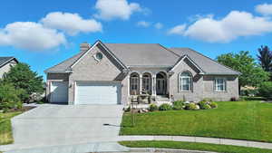 View of front of house featuring an attached garage, brick siding, driveway, and a front lawn