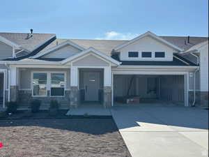 Craftsman-style home featuring concrete driveway, stone siding, and roof with shingles