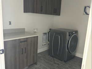 Washroom with cabinet space, washer / dryer, and dark tile patterned flooring