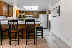 Kitchen with freestanding refrigerator, under cabinet range hood, a peninsula, light countertops, and a skylight