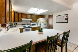 Kitchen featuring white appliances, under cabinet range hood, light countertops, a peninsula, and a breakfast bar area