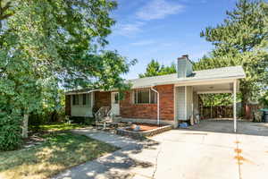 Rambler-Ranch-style home featuring concrete driveway, a chimney, an attached covered carport, and brick siding