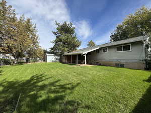 View of green lawn with a sunroom, an outdoor structure, and a patio