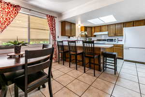 Kitchen with white appliances, a skylight, under cabinet range hood, light tile patterned floors, and crown molding