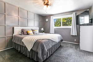 Primary bedroom featuring carpet ,decorative wall, a textured ceiling, and ceiling fan