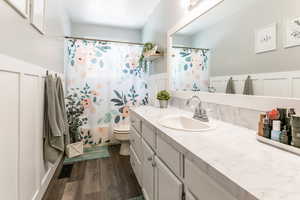 Full bath with vanity, wood finished floors, a wainscoted wall, and a shower/tub with curtain