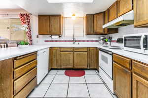 Kitchen with white appliances, under cabinet range hood, light countertops, a textured ceiling, and brown cabinets