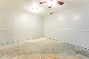 Large room to accommodate many uses, with concrete flooring, ceiling fan, wainscoting, and a textured ceiling