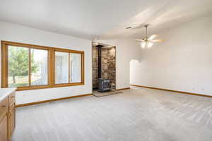 Unfurnished living room featuring light colored carpet, a wood stove, ceiling fan, and lofted ceiling