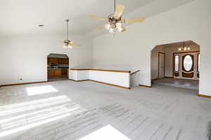 Unfurnished living room featuring arched walkways, a ceiling fan, light colored carpet, and high vaulted ceiling