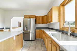 Kitchen with stainless steel fridge, light countertops, light tile patterned floors, and brown cabinets