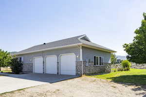 View of side of property featuring driveway, stone siding, a garage, and a shingled roof