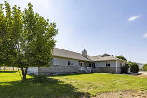 Rear view of property featuring stone siding, a chimney, a lawn, an attached garage, and a shingled roof