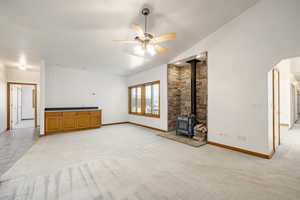 Unfurnished living room featuring a wood stove, ceiling fan, lofted ceiling, light carpet, and arched walkways