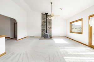 Unfurnished living room featuring a wood stove, carpet, a ceiling fan, high vaulted ceiling, and arched walkways