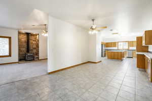 Unfurnished living room featuring ceiling fan, a wood stove, and light colored carpet