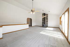 Unfurnished living room featuring a wood stove, light colored carpet, vaulted ceiling, ceiling fan, and arched walkways
