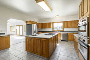 Kitchen with stainless steel appliances, brown cabinets, a kitchen island, light countertops, and light tile patterned floors