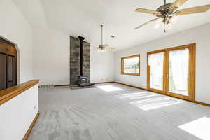 Unfurnished living room featuring a wood stove, carpet floors, ceiling fan, french doors, and high vaulted ceiling