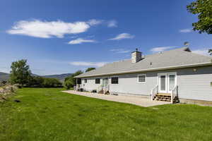 Rear view of house featuring entry steps, a mountain view, a lawn, a chimney, and roof with shingles
