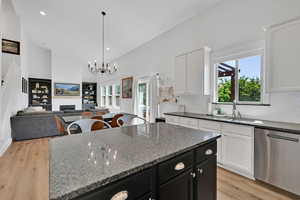 Kitchen featuring stainless steel dishwasher, light wood-style floors, white cabinetry, high vaulted ceiling, and dark cabinets