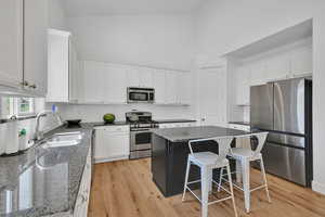 Kitchen featuring appliances with stainless steel finishes, white cabinetry, dark stone counters, a towering ceiling, and tasteful backsplash